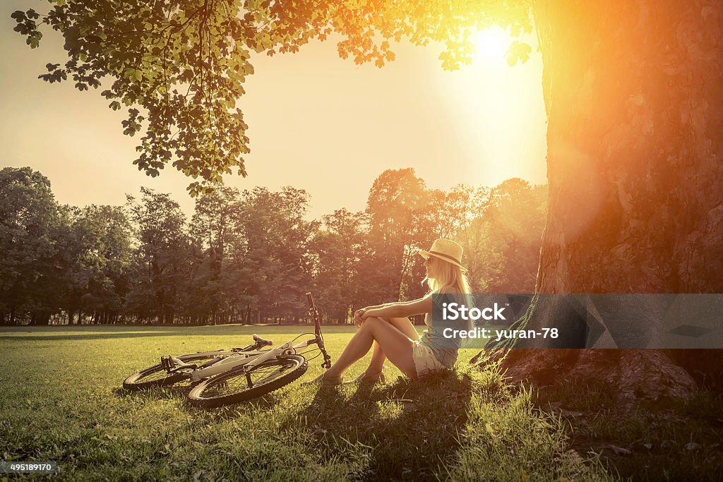 Woman sitting near her bicycle in the park under sun Woman sitting under sun light at day near her bicycle in the park 2015 Stock Photo