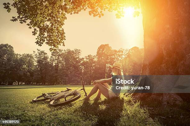 Woman Sitting Near Her Bicycle In The Park Under Sun Stock Photo - Download Image Now