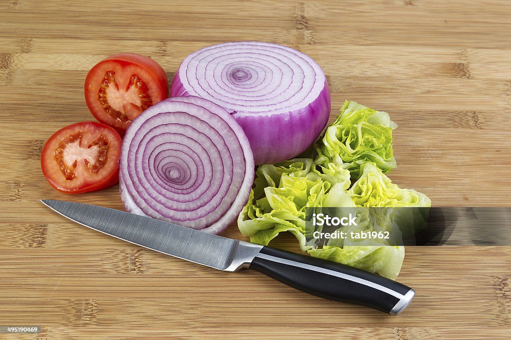 Fresh Tomato, lettuce and Onion on Cutting Board Closeup horizontal photo of freshly sliced red onion, lettuce and tomato with kitchen knife in front and natural bamboo wood underneath Chopped Food Stock Photo