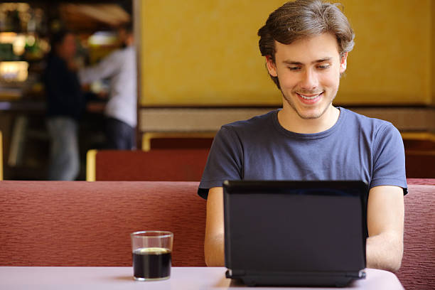 Happy relaxed man browsing social media surfing internet on a laptop in a restaurant