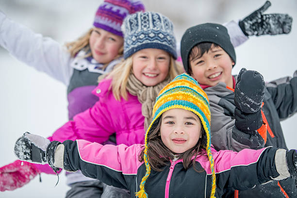 Children Happily Playing in the Snow A multi-ethnic group of elementary age children are playing together in the snow and are smiling while looking at the camera. kids winter coat stock pictures, royalty-free photos & images