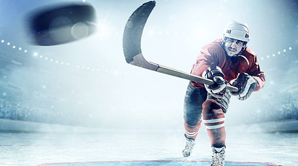 Ice hockey players in action View of professional ice hockey player scoring during game in indoor arena full of spectators taking a shot sport stock pictures, royalty-free photos & images
