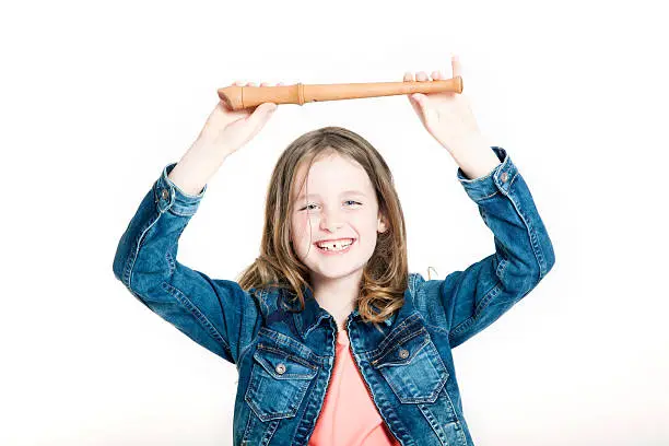 young girl holding up soprano recorder against white background in studio
