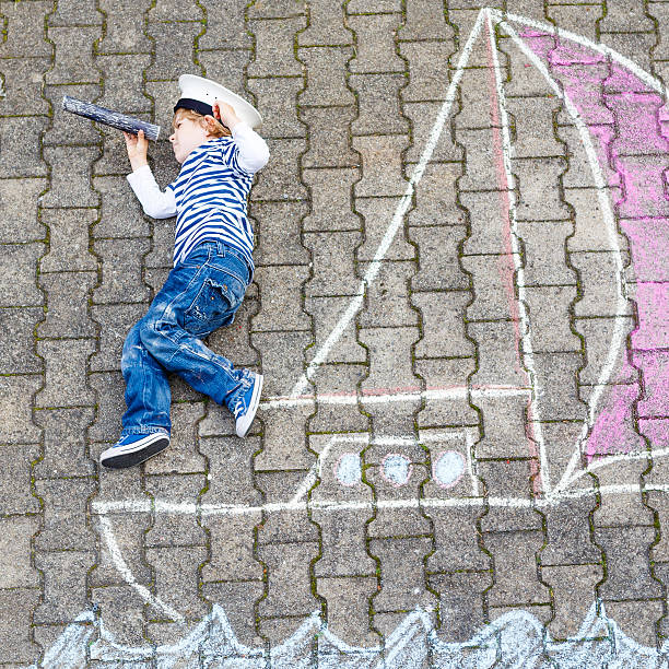 istock Little kid boy  with ship picture drawing with chalk 495230266