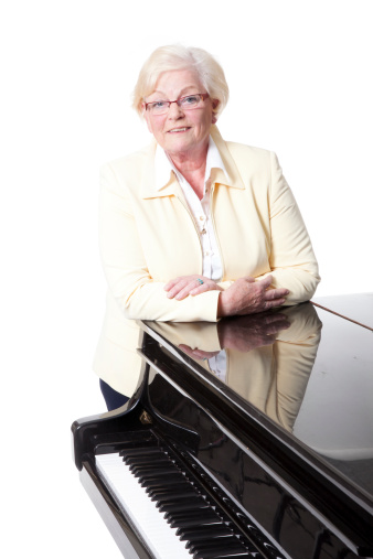 elderly lady in yellow leaning on grand piano in studio with white background