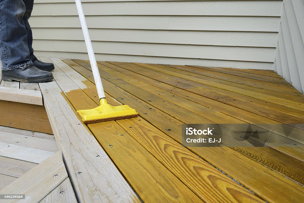 Worker Applying Stain to Deck Painter using sponge applicator to apply stain to deck. Deck Stock Photo