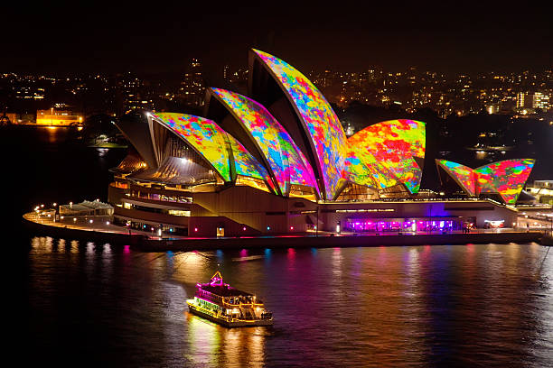 Sydney, Australia - June 1, 2014: A colourfully illuminated boat sails near the Sydney Opera House, as colourful splotches of paint are projected on its sails as part of the Vivid Sydney festival.