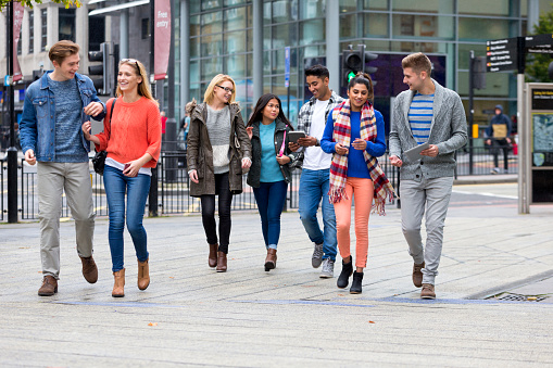 Group of mixed ethnic university students happily walking through town after their studies. Happily together with their digital tablets.
