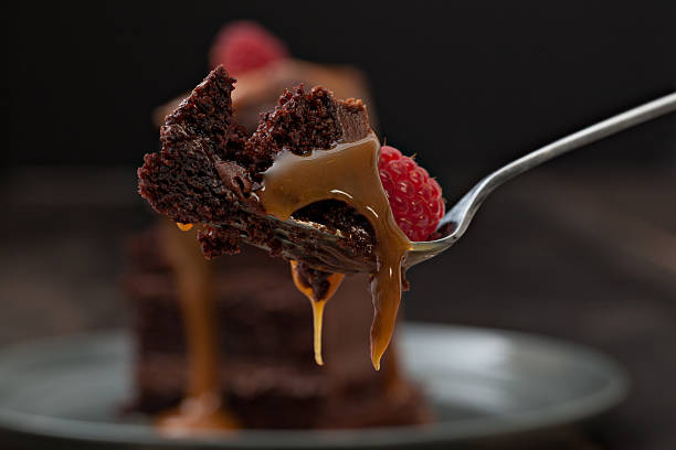 Bite Of Chocolate Cake An extreme close up horizontal photograph of a piece of chocolate fudge cake on a fork dripping golden brown caramel sauce, isolated on black. indulgence stock pictures, royalty-free photos & images