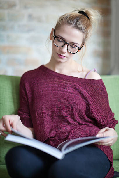 istock Young woman reading a book at home 495252256