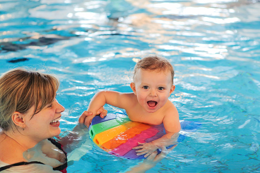 Happy young mother and little baby swimming in indoor pool. Healthy childhood and growth of children