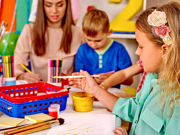 istock Kids with teacher holding colored paper and glue on table 495273900