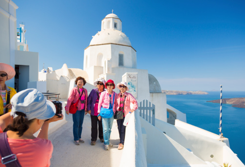 Fira, Greece - May 24, 2014: Group of mature asian women posing for a group vacation photo in front of a small church in Fira on Santorini island in Greece.