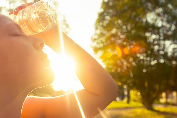 Woman using water bottle to cool down. Woman using water bottle to cool down. Fitness and wellbeing concept with female athlete cooling down on a city street. She is holding a water bottle to her head to cool down. The sun is low creating long shadows and some lens flare. Copy space hot women working out pictures stock pictures, royalty-free photos & images