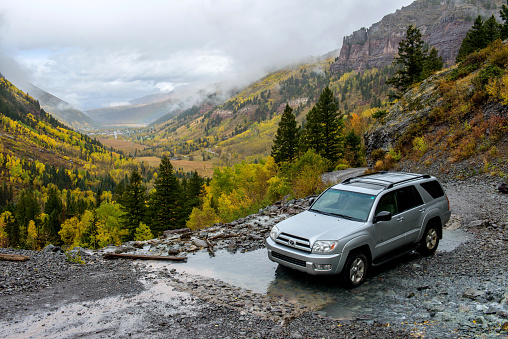 Telluride, Colorado, USA - October 05, 2015: it's a rainy and foggy autumn day, a SUV is driving through a mountain creek on the rugged Black Bear Pass trail -- the only way to the top of the Bridal Veil Falls. The town of Telluride is in the background.