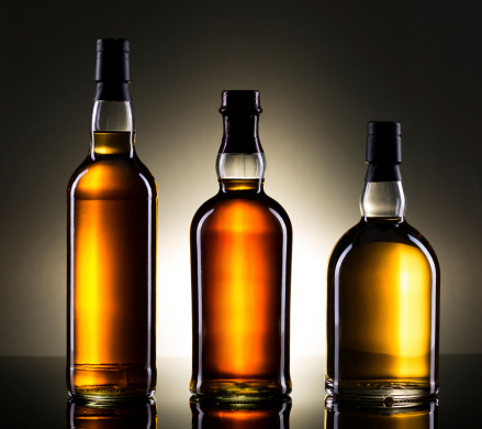 Three bottles of whiskey on reflective surface.