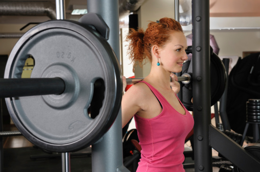 young red haired girl doing squats with barbell on smith machine