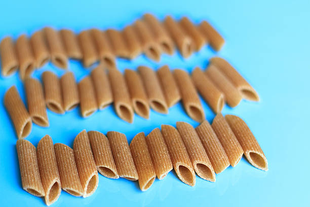 Uncooked Whole Wheat Penne Pasta Lined Up on Blue Background
