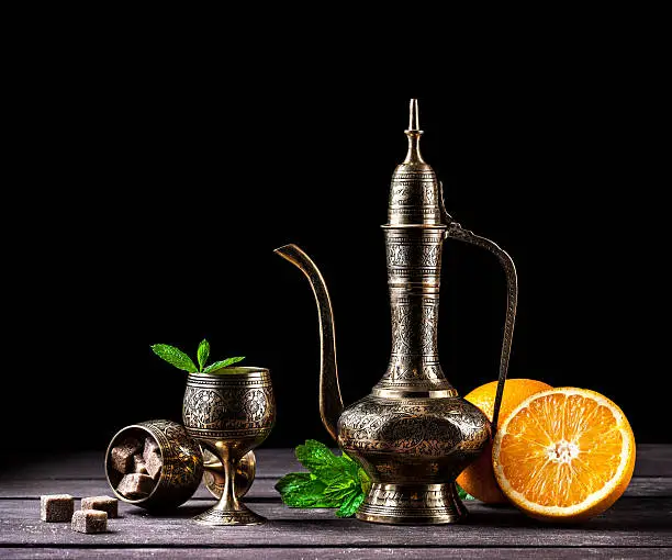 Moroccan tea with mint and oranges in oriental cooper pot and cups on rustic wooden background