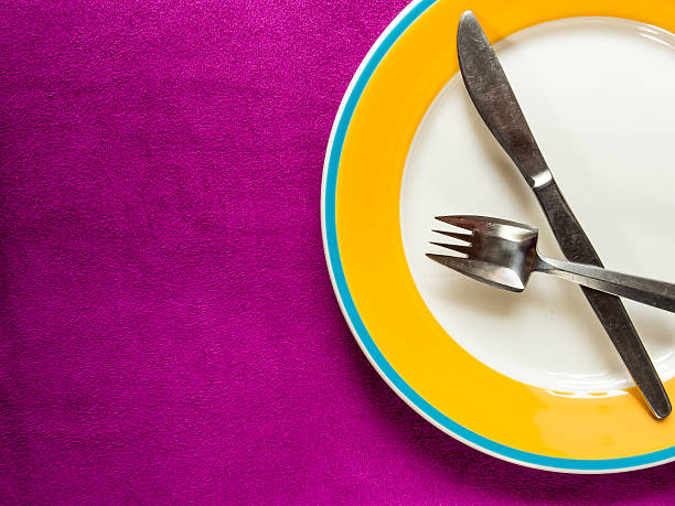 istock Empty Plate with fork and knife on purple fabric background 495333699