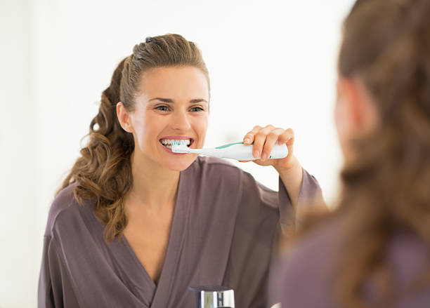 young woman brushing teeth in bathroom stock photo