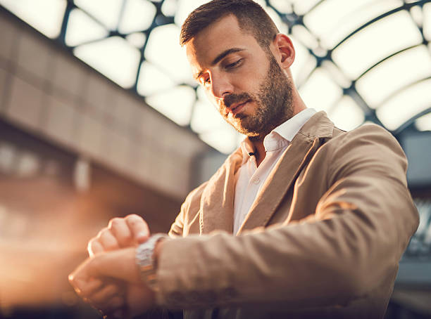 Serious businessman standing outdoors and checking the time on his watch.