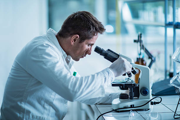 masculino forense cientista analisar algo em um microscópio. - genetic research men chemical protective glove - fotografias e filmes do acervo