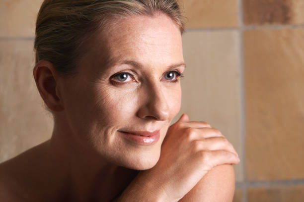A mature woman with bare shoulders looking away against a beige background