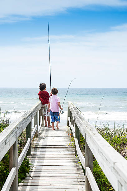 Brothers ready to go surf fishing in North Carolina. Two brothers heading to the beach on the Outer Banks of North Carolina to go surf-fishing on vacation. sea fishing stock pictures, royalty-free photos & images