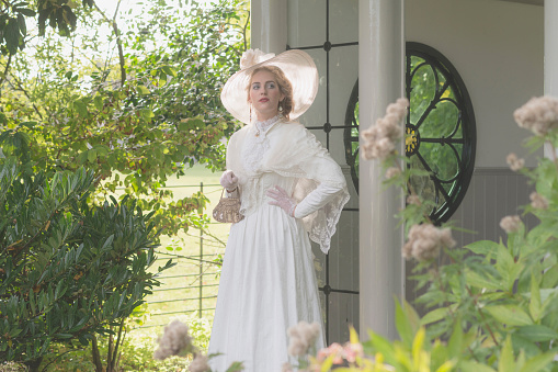 Vintage posh victorian woman with hat standing in bower.