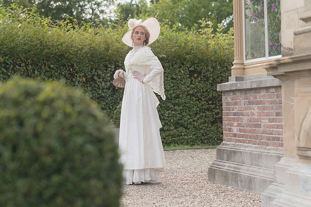 Posh victorian woman with hat standing in garden.