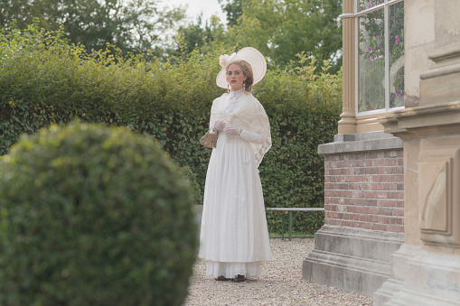 Posh victorian woman with hat standing in garden.