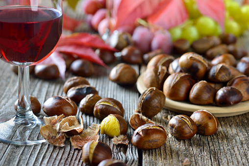 Roasted chestnuts with South Tyrolean red wine on an old wooden table, wine grapes in the background
