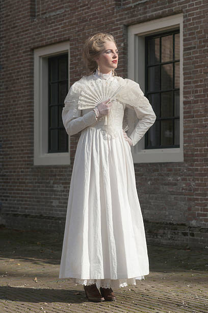 Victorian woman with fan standing in front of building.