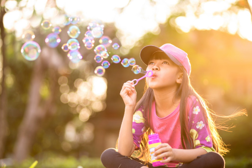Little asian girl blowing soap bubbles outdoor at sunset