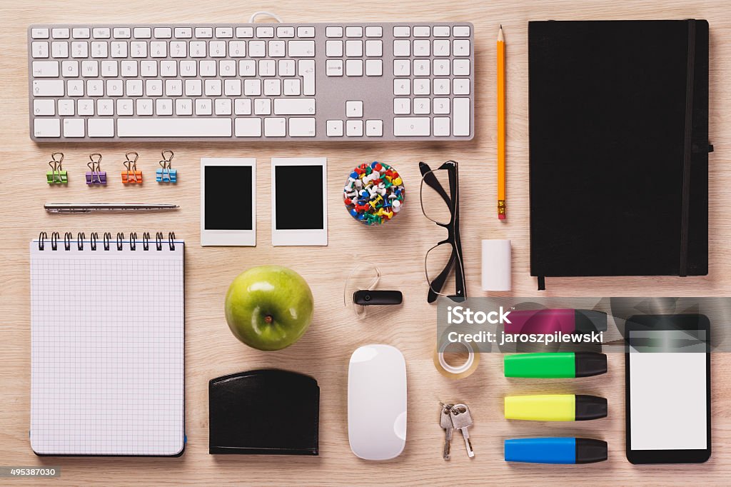 Top of desk with office equipment arranged if perfect order. Bright office wooden desk with computer keyboard, mouse, photos, calendar, pencil, highlighters, smart phone, note pad, wallet, apple and other office equipment arranged in perfect order. Neat Stock Photo