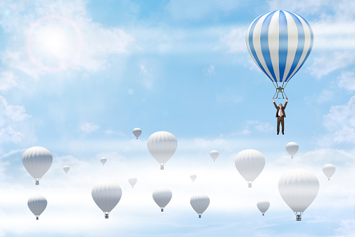 Businessman holding balloon among other white balloons in sky