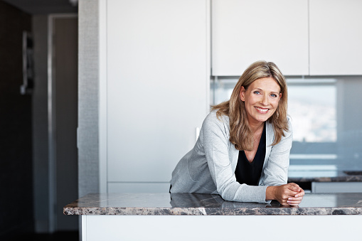 Portrait of a smiling mature woman leaning on her kitchen countertop