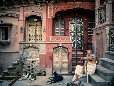 Bikaner, India - September 30, 2015: Senior man with dogs sitting in front of an old beautiful house in Bikaner Rajasthan India.  It was once the capital of the princely state of Bikaner. It was founded by Rao Bika in 1486. It is now the fourth biggest city in Rajasthan and although not receiving as many tourists as other cities in the state it is slowly gaining popularity because of the beautiful havelis (houses) an amazing fort palaces and temples.