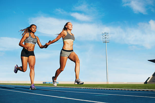 Female relay racing team on racetrack Young woman running a relay race and giving relay baton to her teammate. Female runner passing the relay baton during race. relay photos stock pictures, royalty-free photos & images