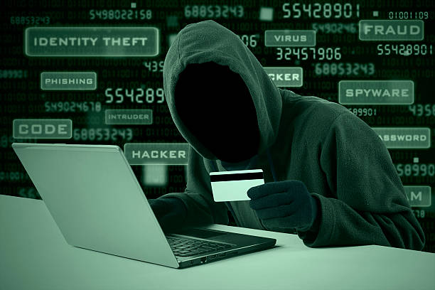Hacker stealing credit card number Internet Theft - a man wearing a balaclava and holding a credit card while sat behind a laptop, gangster photos stock pictures, royalty-free photos & images