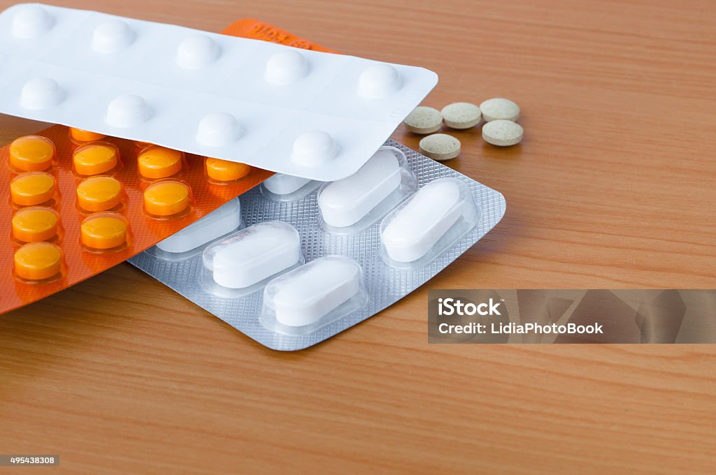 Blister packs of tablets on table Photo shows blister packs of pills and five pills laying separatey on the table. Light is close to natural. Drugs and medicaments are nameless. Objects in the picture are in the left right corner. 2015 Stock Photo