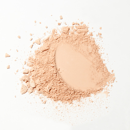 make up close up of a crumbled and scattered natural color powder on white background