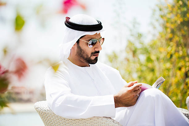 Relaxin and reading in a Dubai garden. One young man is reading a book while sitting on his garden. arabian sunglasses stock pictures, royalty-free photos & images