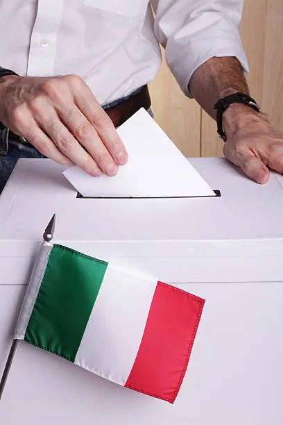A man inserting a ballot to a ballot box.  Italian flag in front of it.
