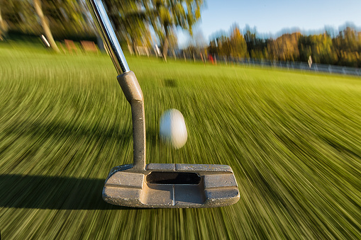 Panning shot of golf ball coming up to the hole, blurred background with blue sky, shallow depth of field