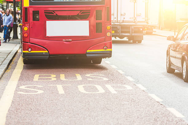 Red double-decker bus at bus stop in London. View from back, with focus on BUS writing on the road. on the left there are some persons and on the right some vehicles. Urban transport concept.