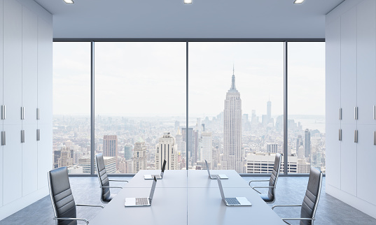 Workplaces or conference area in a bright modern open space office. White tables equipped by modern laptops and black chairs. New York view. 3D rendering.