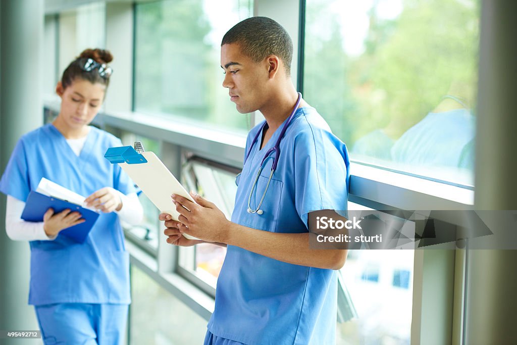 two young nurses on the ward a young male and female nurse stand in the corridor of the hospital checking their medical notes . Junior Doctor Stock Photo