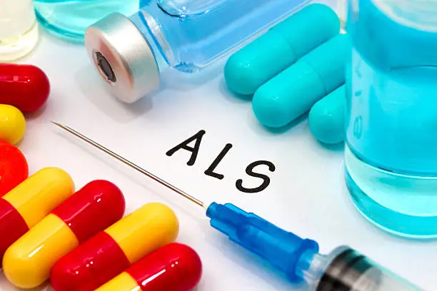ALS - diagnosis written on a white piece of paper. Syringe and vaccine with drugs.